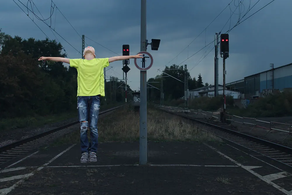 A child stand with their arms outstretched on train tracks at night.
