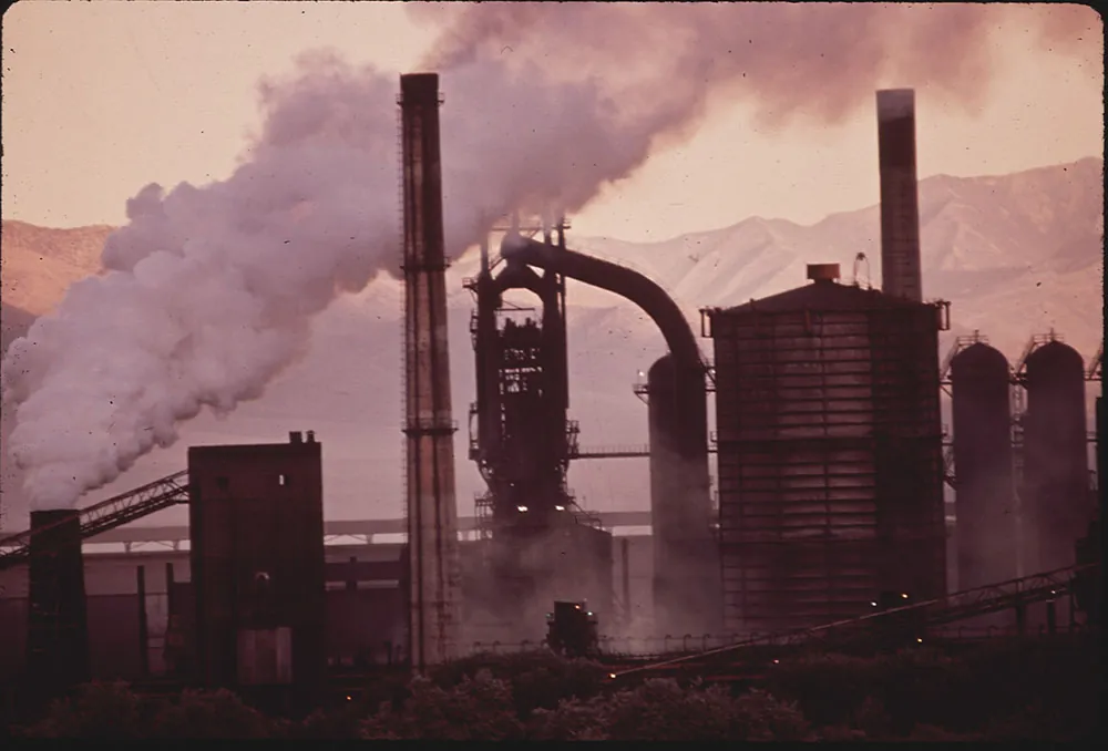 an old steel mill at sunrise with smoke rising out of a smoke stack.