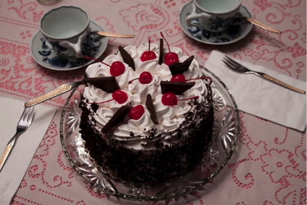 Photo of a chocolate cake with cherries and whipped cream on top.