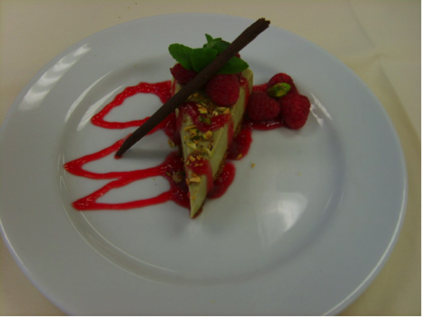 Photo of a slice of cheesecake on a white plate with red drizzle.