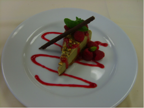 Photo of a slice of cheesecake on a white plate with red drizzle.