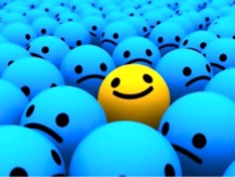 Photo of a bunch of unhappy blue balls with one yellow happy ball in the middle