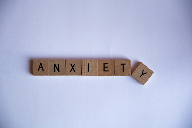 "Seven wooden Scrabble tiles on a white background spell the word 'ANXIETY.' The first six tiles are aligned horizontally, while the final tile with the letter 'Y' is slightly tilted at an angle."