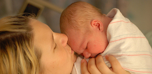 "Photo of a an adult and a baby. The adult appears to be giving the baby a kiss on the head"