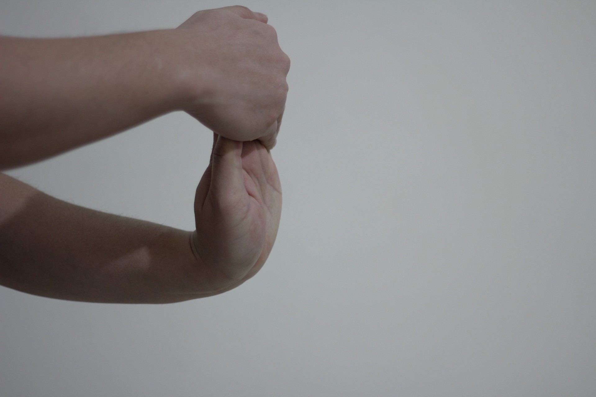 "A close-up of a person's hands against a plain background. One hand is stretching the fingers of the other hand backward, demonstrating a wrist and finger stretch."