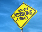 "A yellow diamond-shaped road sign reads 'TOUGH DECISIONS AHEAD' against a blue sky background."