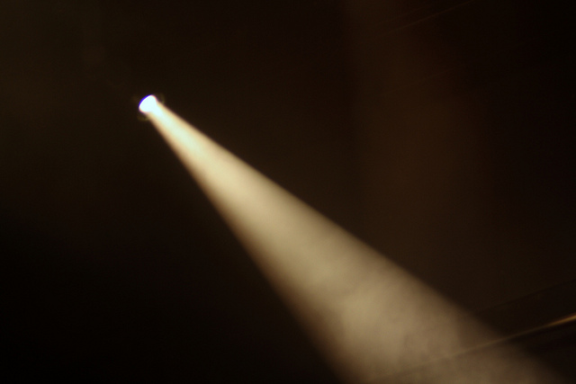 "A single spotlight shines brightly in a dark, smoky environment, creating a focused beam of light that cuts through the darkness."