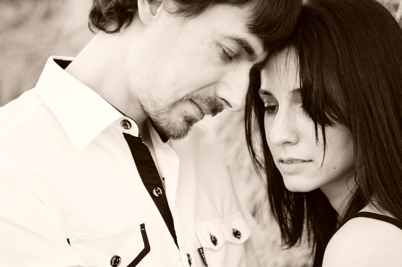 "A sepia-toned photograph of two people standing close together. The person on the left is wearing a light-colored button-up shirt with dark buttons and pockets. The person on the right has long dark hair."