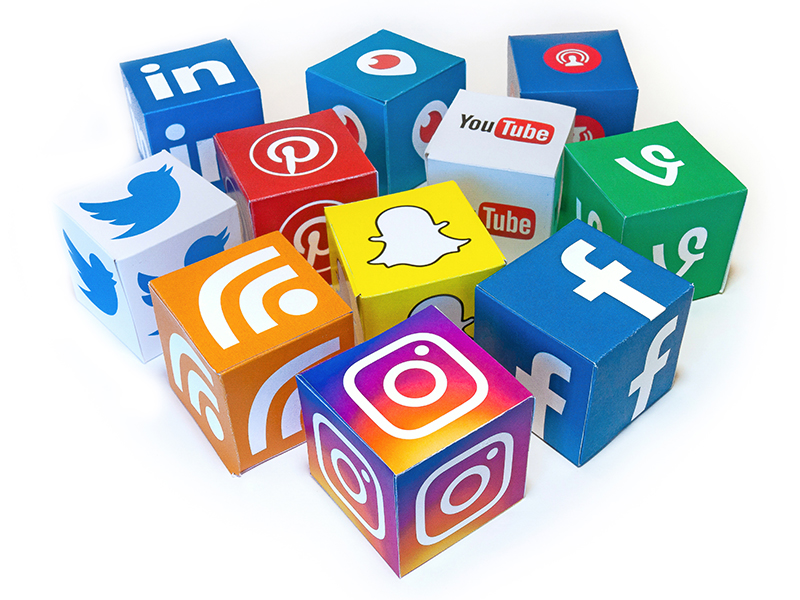 A collection of colorful paper cubes, each displaying the logo of a popular social media platform. Visible logos include LinkedIn, Twitter, Pinterest, Snapchat, Instagram, Facebook, YouTube, Vine, and RSS. The cubes are arranged in a semi-circle on a white surface, showcasing the variety of platforms in a playful and vibrant manner.