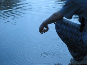 Partial image of a person squatting down next to a body of water. 