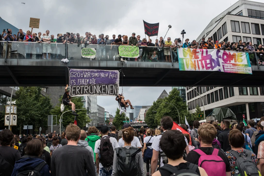 Photo of a street and bridge filled with people protesting and hanging signs.