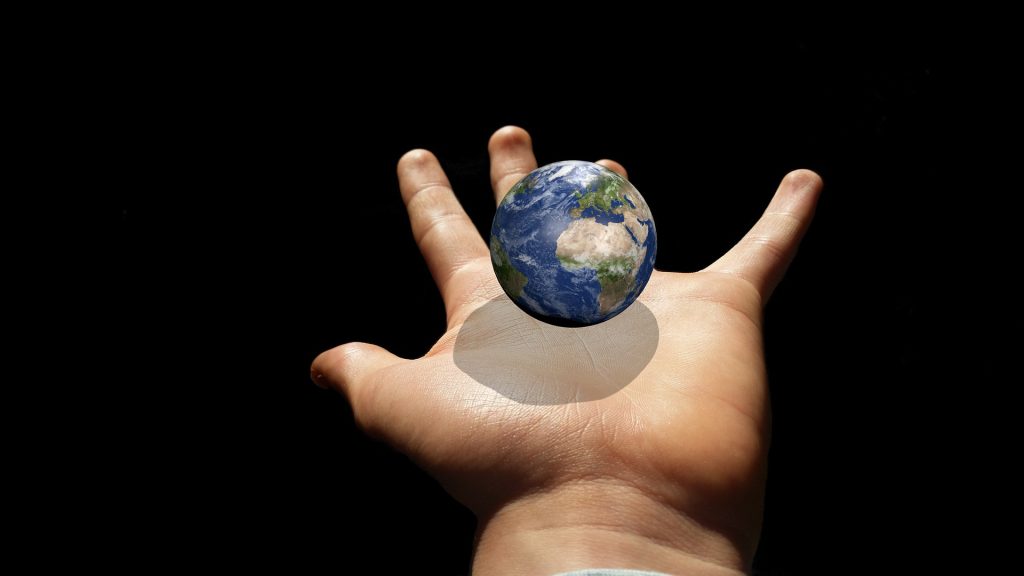 Photo of a hand with a small globe hovering over the palm. 